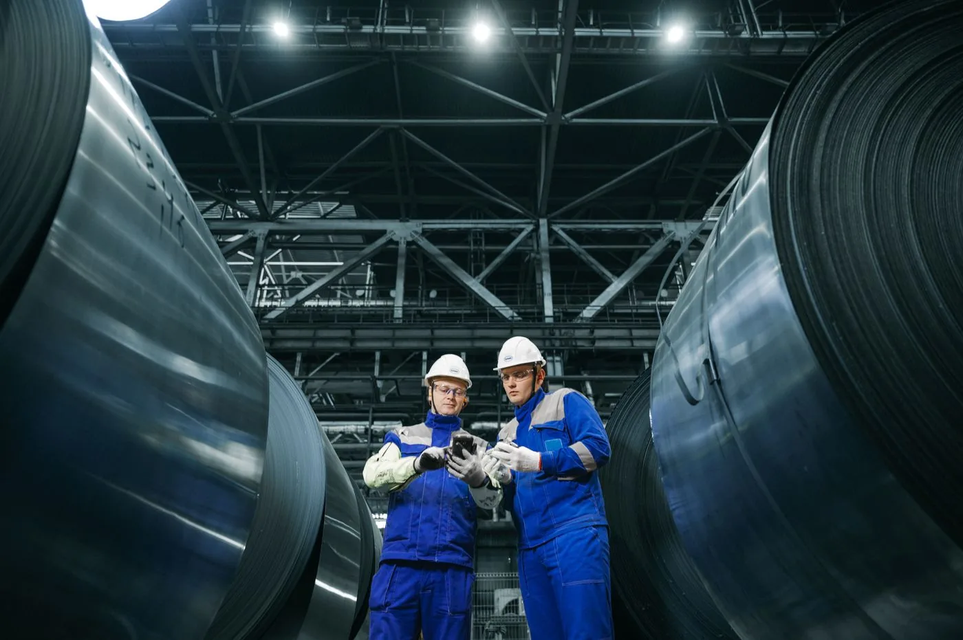 Workers wearing hard hats reviewing a device in a steel manufacturing facility