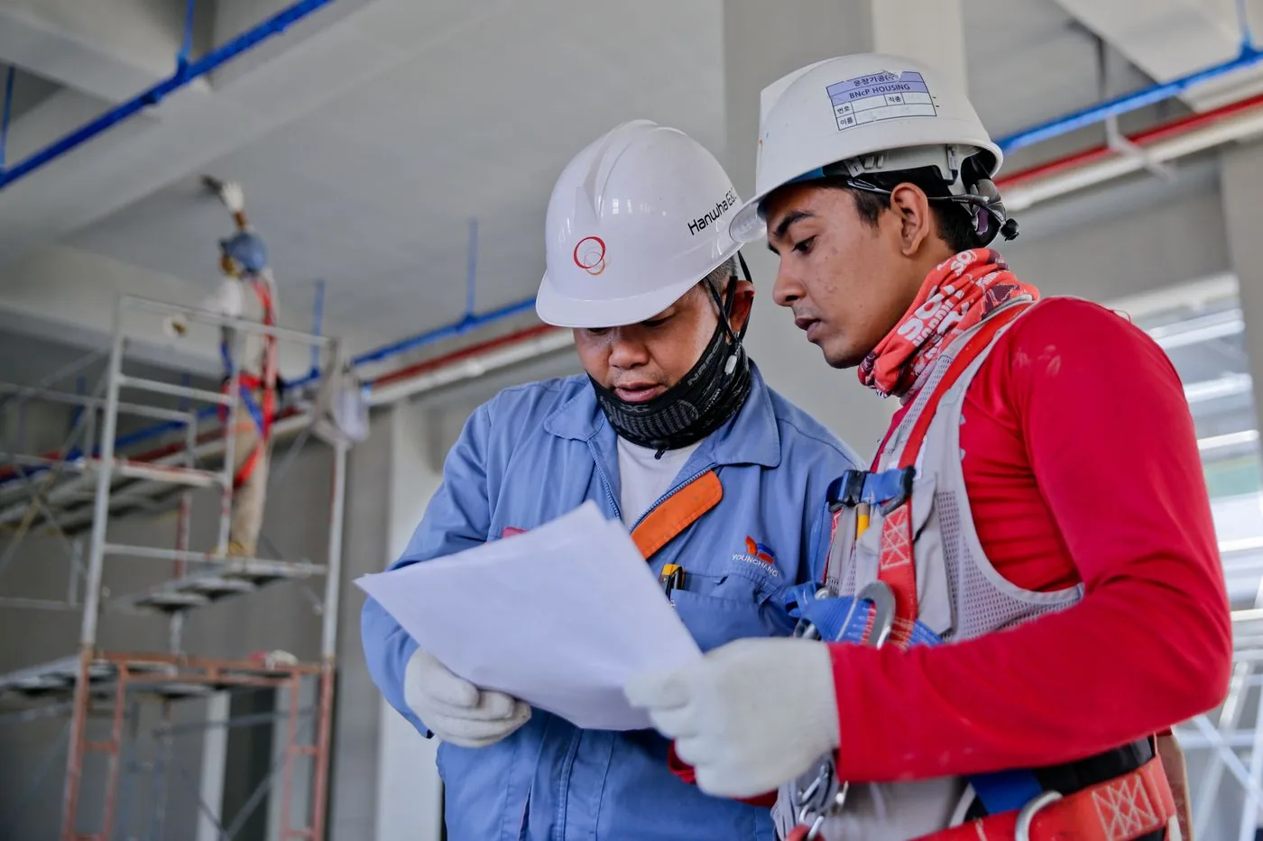 Two site professionals in hard hats reviewing plans together inside a building